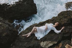 lindo mulher dentro uma isolado local em uma selvagem rochoso costa dentro uma branco vestir inalterado foto