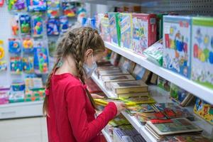 krasnodar, Rússia marcha 7, 2021. uma criança dentro uma médico mascarar é escolhendo uma crianças brinquedo dentro a loja. uma menina é compras em meio a a covid-19 pandemia. foto