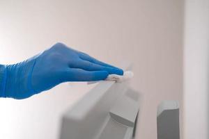 uma masculino mão dentro borracha luvas lenços a poeira a partir de uma computador monitor com uma guardanapo. desinfecção às lar, limpeza dentro a contexto do a covid-19 pandemia. foto