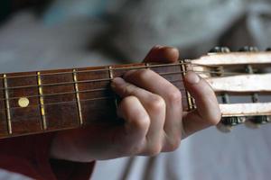 cara toca uma melodia em um violão enquanto segura sua mão no braço da guitarra
