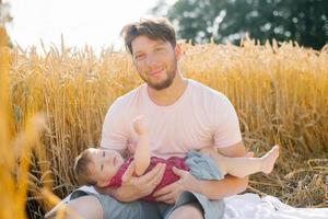 uma jovem Papai e dele filho estão sentado dentro natureza dentro a verão dentro a campo. foto