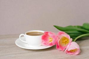 café com leite dentro uma branco porcelana copo e pires, uma ramalhete do Primavera Rosa tulipas. mãe dia, dia dos namorados dia, Páscoa. a conceito do Primavera foto