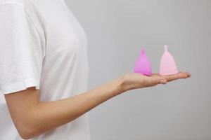 copo menstrual rosa. close-up da mão de uma mulher segurando copos menstruais de diferentes tipos. conceito de saúde da mulher, alternativas de desperdício zero foto