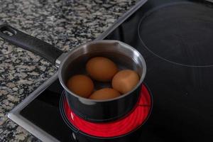 ovos dentro uma aço alumínio Panela estão cozinhou em a elétrico fogão foto