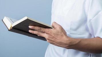 muçulmano homem lendo piedosos livro Alcorão, isolado em azul fundo foto