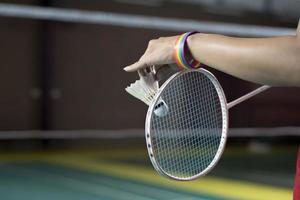 badminton jogador desgasta arco Iris pulseiras e segurando raquete e branco peteca dentro frente do a internet antes servindo isto para jogador dentro outro lado do a tribunal, conceito para lgbt pessoas Atividades. foto