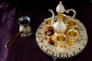 natureza morta com tradicional café árabe dourado com dallah, cafeteira e tâmaras. fundo escuro. foto vertical