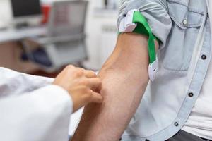 preparação para sangue teste de fêmea médico médico uniforme em a mesa dentro branco brilhante sala. enfermeira pierces a pacientes braço veia com agulha em branco tubo. foto