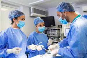 equipe diversificada de cirurgiões profissionais, assistentes e enfermeiras realizando cirurgia invasiva em um paciente na sala de cirurgia do hospital. cirurgiões falam e usam instrumentos. verdadeiro hospital moderno. foto