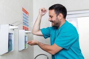 médico lavando mãos com sabão. masculino cirurgião é preparando para cirurgia. ele é dentro uniforme foto