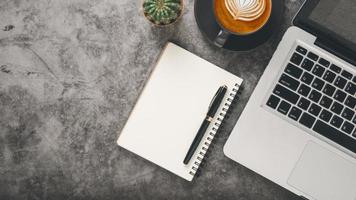 Sombrio escritório escrivaninha local de trabalho com computador portátil computador, caderno, caneta e copo do café, topo Visão plano deitar com cópia de espaço. foto