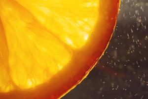 laranja fatia macro com uma solta do água fundo . suculento laranja fatiado fechar-se em uma Sombrio fundo foto