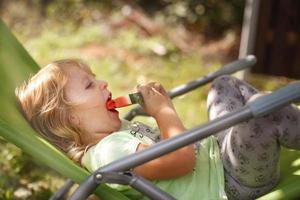 fofa pequeno menina comendo Melancia em uma área coberta cadeira dentro a jardim dentro horário de verão foto