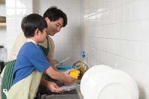 feliz sorridente jovem ásia pai e filho lavando pratos dentro cozinha às casa foto