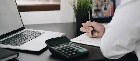 profissional fazendo anotações com calculadora e laptop na mesa foto