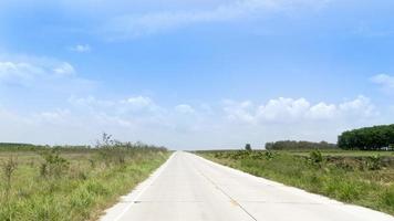 país concreto estrada dentro tailândia. ensolarado estrada em a aberto espaço do a Prado dois ao lado do estrada. debaixo a azul céu e branco nuvens. foto