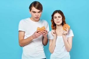 jovem casal dentro branco Camisetas com hambúrgueres dentro seus mãos velozes Comida lanche foto
