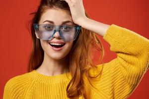 alegre mulher dentro amarelo suéter azul óculos posando estúdio foto