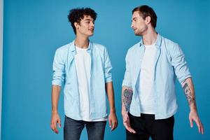 dois amigos dentro a desabotoado camisa e dentro branco Camisetas em uma azul fundo gesticulando com mãos cortada Visão festa foto