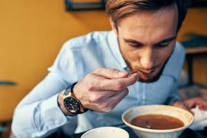 uma homem come borscht com azedo creme dentro uma restaurante às uma mesa dentro uma cafeteria e uma Assistir em dele mão foto
