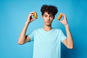 homem com encaracolado cabelo laranjas segurando fruta estúdio azul fundo foto