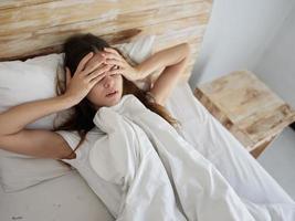 mulher mentiras dentro cama coberto com uma cobertor mãos em dela face dentro a manhã foto