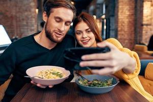 jovem casal dentro uma restaurante faz uma selfie em a telefone comunicação foto