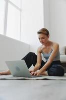 freelance mulher com computador portátil e telefone trabalho a partir de casa sentado em a chão dentro dela casa roupas com uma curto corte de cabelo, livre cópia de espaço foto