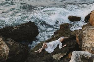 atraente mulher com grandes cabelo deitado em rochoso costa com rachaduras em rochoso superfície período de férias conceito foto
