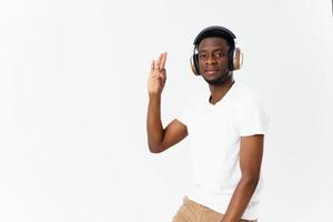 africano americano dentro fones de ouvido dentro uma branco camiseta escuta para música mão gesto luz fundo foto