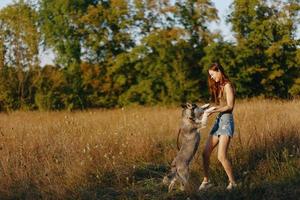 uma mulher tocam e danças com uma rouco procriar cachorro dentro natureza dentro outono em uma campo do Relva e sorrisos às uma Boa tarde dentro a configuração Sol foto