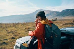 mulher dentro uma Jaqueta com uma mochila e uma boné carrinhos perto a carro em natureza dentro a montanhas dentro verão foto