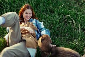 mulher deitado em a Relva sorridente jogando e abraço dela cachorro dentro natureza dentro a parque dentro a verão pôr do sol. a conceito do saúde e amor do animais, tratamento do carrapatos e pulgas Relva e animais foto