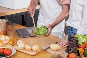 jovem ásia casal cozinhando com frutas e legumes e usando computador portátil dentro a cozinha para cozinhar Comida juntos dentro a família Felizmente, família conceito. foto