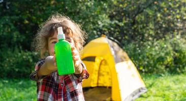 menina pulveriza spray de mosquito na pele na natureza que morde as mãos e os pés. proteção contra picadas de insetos, repelente seguro para crianças. recreação ao ar livre, contra alergias. horário de verão foto