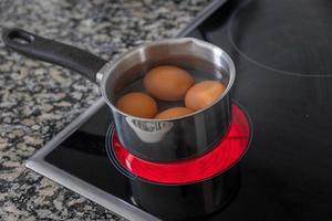 ovos dentro uma aço alumínio Panela estão cozinhou em a elétrico fogão foto