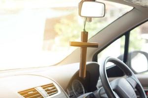 closeup crucifixo de madeira pendurado no volante dianteiro e console do carro. conceito, talismã, amuleto para evitar acidentes. crença, fé, santo em Deus para proteger ao dirigir. foto