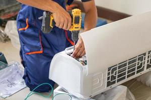 ásia técnico homem instalando a ar condicionamento dentro uma cliente casa, jovem reparador fixação ar condicionador unidade, manutenção e reparação conceitos foto