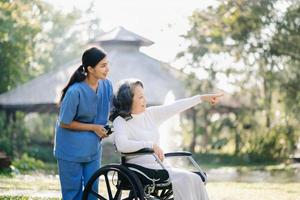 idosos ásia Senior mulher em cadeira de rodas com ásia Cuidado cuidador. enfermagem casa hospital jardim conceito. dentro luz solar foto