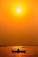 tarde dourado pôr do sol tempo, uma pescador pescaria em a beira-mar em uma barco. foto