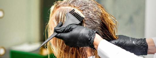 mão do uma cabeleireiro dentro Preto luvas aplicando corante para a fêmea cabelo dentro uma beleza salão. foto