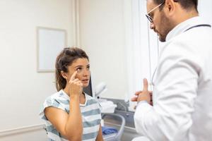 mulher tendo uma olho problema e dor. médico trabalhando dentro a escritório e ouvindo para a paciente, ela é explicando dela sintomas, healtcare e assistência conceito foto