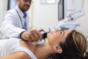 médico fazer ultrassom do tireoide glândula para mulher paciente dentro clínica. diagnóstico e tratamento do autoimune tireoidite conceito foto
