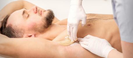 jovem caucasiano homem recebendo cabelo remoção a partir de dele axila dentro uma beleza salão, depilação masculino axila. foto