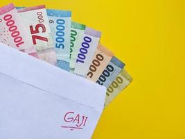 Novo notas emitido dentro 2022 a partir de Rp.1.000 para 100.000 rp. indonésio rupia moeda com uma branco envelope etiquetado gaji. Tunjangan hari raya conceito isolado em amarelo fundo. foto