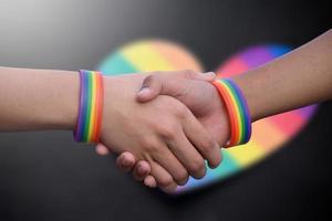 fechar-se Visão do aperto de mãos do lgbt pessoas com borrado arco Iris fundo, conceito para sucesso, cooperação, reconciliação, confiar, e amor para lgbt pessoas e celebrações dentro orgulho mês. foto