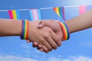 fechar-se Visão do aperto de mãos do lgbt pessoas com borrado arco Iris fundo, conceito para sucesso, cooperação, reconciliação, confiar, e amor para lgbt pessoas e celebrações dentro orgulho mês. foto