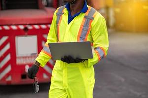 fechar acima técnico doca trabalhador dentro protetora segurança macacão uniforme e com capacete de segurança e usar computador portátil computador às carga recipiente Remessa armazém. transporte importar, exportar logístico industrial foto