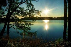 dramático lituano lago Plateliai em nascer do sol. azul lago Relva e manhã caloroso ensolarado fundo. Sol flare dentro a manhã acima a lago. foto