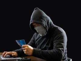 hacker espião homem uma pessoa com capuz preto sentado em uma mesa olhando computador laptop usado segurança de ataque de senha de login para circular dados digitais no sistema de rede da internet, fundo escuro noturno. foto